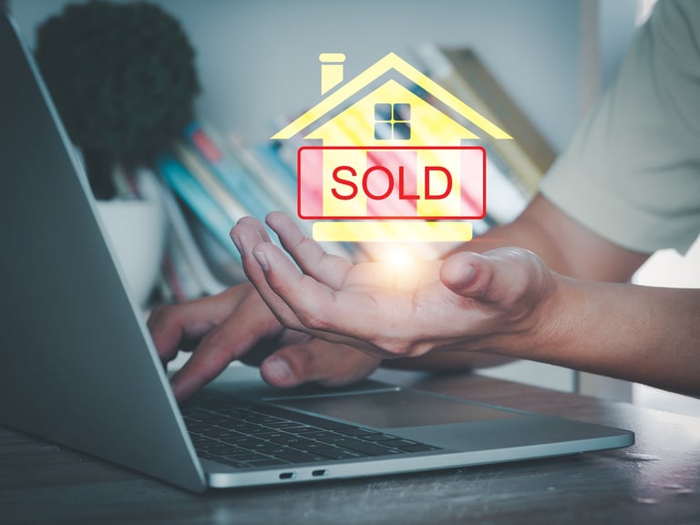 Person using laptop with digital house icon and sold sign, symbolizing real estate transaction