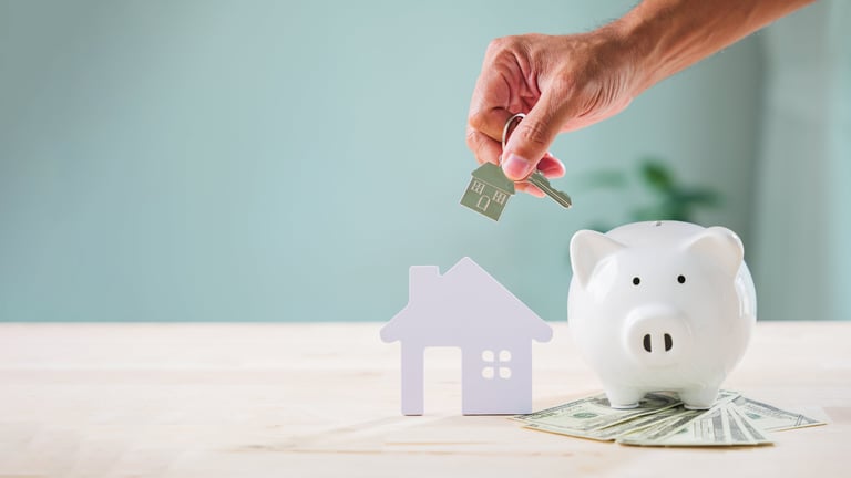 Hand offers house key above paper home model for bank piggy saving security