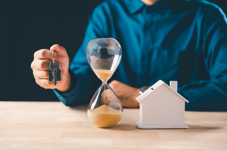 Hand holds real estate house keys, hourglass with falling sand marks time, symbolizing mortgage deadline